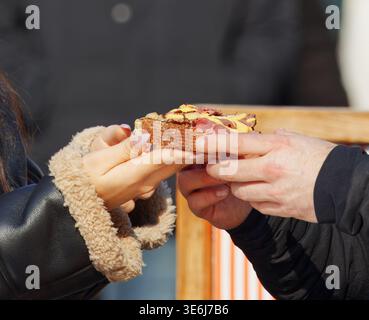 Nahaufnahme eines Paares, das sich ein köstliches Pastrami- und Senfsandwich auf dem Naplavka Bauernmarkt in Prag teilt. Perfekt für Street Food, Dating und Outd Stockfoto