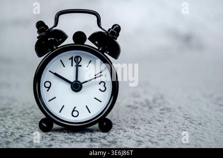 Sauber gerahmtes schwarzes Wecker-Produkt, das einen späten Morgenmoment um zehn Uhr auf einem hellen, strukturierten Hintergrund darstellt. Stockfoto