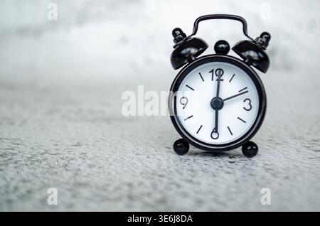 Minimales Miniaturbild für den Wecker in Schwarzweiß, das ein frühmorgendliches 6-Uhr-Konzept auf einem strukturierten grauen Hintergrund zeigt. Stockfoto