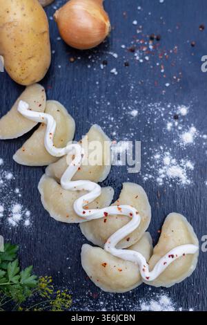 Vertikaler Schuss von handgemachten Knödeln oder Pierogi mit einem Schuss Sauerrahm auf schwarzem Schiefer. Authentische traditionelle Mahlzeit. Stockfoto