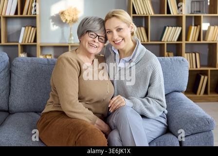 Glückliche Seniorenmutter und Erwachsene Tochter umarmen sich auf einem gemütlichen Heimsofa, Familienliebe Stockfoto