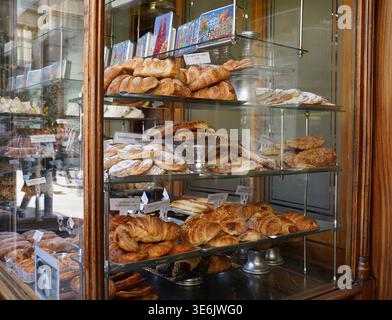Blick von der Straße durch ein altes Holzfenster mit Brot, Croissants, Gebäck und süßen Leckereien zum Verkauf in Barcelona Spanien. Stockfoto