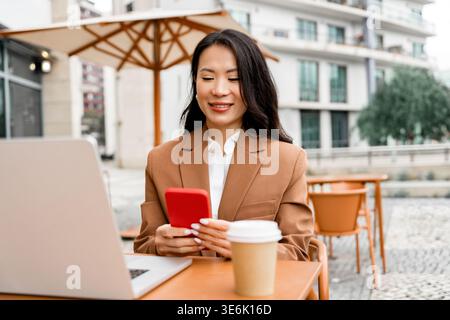 Geschäftsfrau mit Smartphone und Laptop im Café im Freien Stockfoto