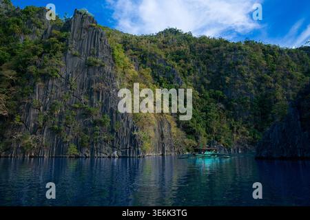 Ein türkisfarbenes Auslegerboot segelt an riesigen Karstkalkfelsen in einer ruhigen tropischen Lagune in Palawan vorbei. Stockfoto