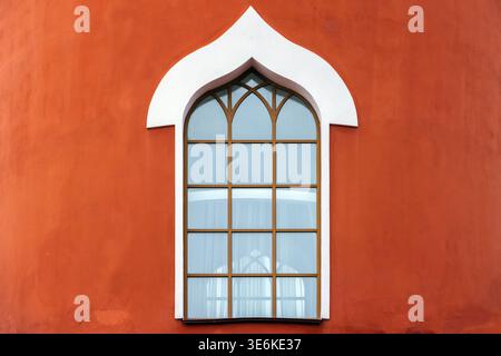 Ein kunstvoll verziertes Bogenfenster mit weißer Zierleiste in einer terrakottafarbenen Fassade, mit geometrischen Pfosten und weichem blauem Glas, das eine ruhige, Mini-Atmosphäre schafft Stockfoto