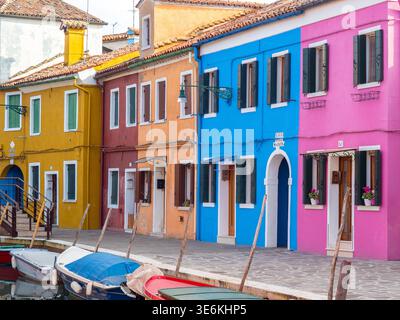 Lebhafte Reihe von bemalten Häusern und vertäuten Booten entlang eines ruhigen Kanals, die Charme, Reisen und mediterrane Farbe in einem historischen Fischerdorf wecken. Stockfoto