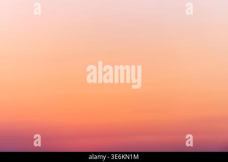 Ein glatter, verlaufender Himmel mit einem Übergang von tiefem Orange zu sanftem Rosa und sanften violetten Tönen, der eine ruhige Ruhe und natürliche Schönheit des Abends darstellt Stockfoto