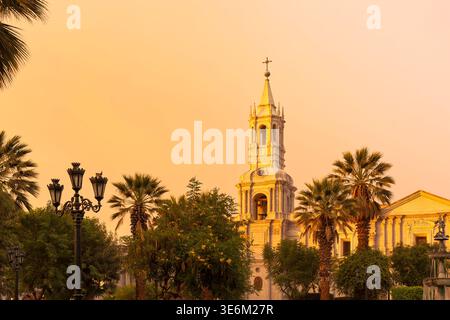 Die weiße vulkanische Steinfassade und der kunstvoll verzierte Glockenturm der Basilika von Arequipa leuchten unter einem warmen Sonnenuntergang in Peru. Stockfoto