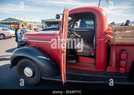 Roter Oldtimer Chevrolet Pickup Truck mit offener Tür, geparkt auf einem Flughafenaspel bei einer Outdoor-Autoshow, umgeben von Menschen, Oldtimern und Hangars u Stockfoto