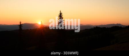 Sonnenuntergang über dem Berghorizont mit warmer Sonne und dunklen Silhouetten im Vordergrund. Ruhige abendliche Landschaft mit sanftem Himmel und natürlicher ruhiger Stimmung Stockfoto