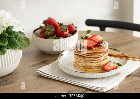 Einladende Frühstückskomposition mit einem Stapel goldener Pfannkuchen mit frischen Erdbeeren und Sirup, serviert auf einem weißen Teller Stockfoto