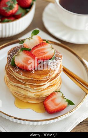 Einladende Frühstückskomposition mit einem Stapel goldener Pfannkuchen mit frischen Erdbeeren und Sirup, serviert auf einem weißen Teller Stockfoto