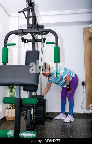 Frau passt Gewichte auf einem funktionalen Heimtrainer an und beginnt ein Workout Stockfoto
