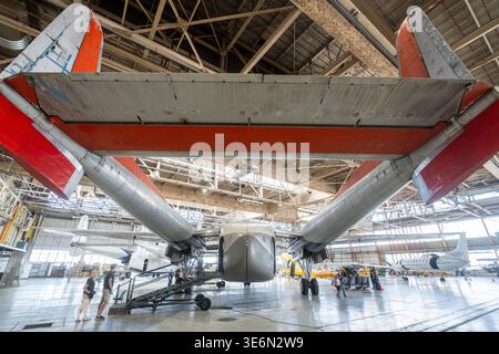 Weitwinkelansicht eines alten zweimotorigen Flugzeugs, das in einem geräumigen Flughafenhangar geparkt ist, mit Besuchern und Bodenausrüstung in der Nähe Stockfoto