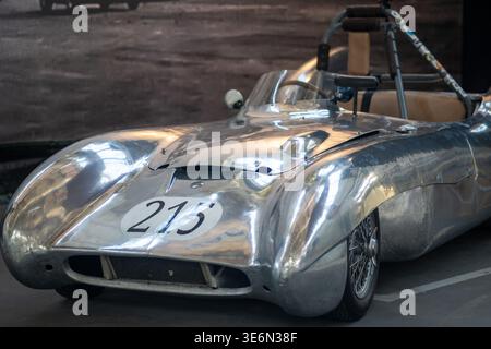 Oldtimer-Rennwagen aus poliertem Aluminium mit offenem Cockpit und Rennnummer 213 in musealer Atmosphäre. Reflektierende Metallverkleidung, Drahtspitze Stockfoto