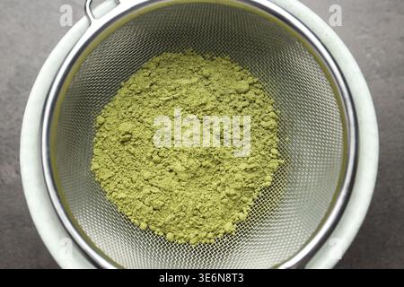 Matcha-Pulver in eine Schüssel am grauen Tisch, Nahaufnahme Stockfoto