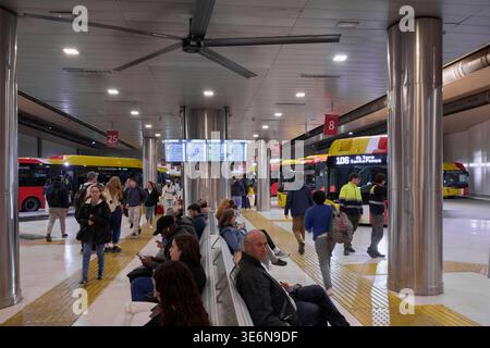 Mallorca. Spanien - 07. April 2026: Pendler sitzen auf Bänken am Bahnhof Palma Intermodal. Ein digitales Abfahrtstafel zeigt die Busfahrpläne oben an Stockfoto