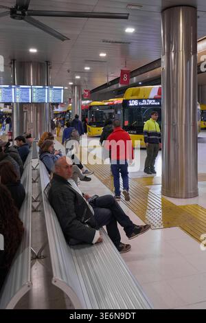 Mallorca. Spanien - 07. April 2026: Pendler sitzen auf Metallbänken am Bahnhof Palma Intermodal nahe der Buslinie 106 nach Santa Ponca. Digitale Abfahrt Stockfoto
