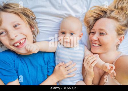 Mutter liegend mit zwei Söhnen, neugeborenem Baby und älterem Kind zu Hause. Liebevolle Familie, die Zeit miteinander verbringt, sich verbindet und entspannt. Mutterschaft Stockfoto