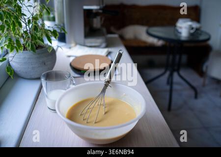 Schüssel mit Teig auf Fensterbank in der Nähe der Pflanze, sanftes Tageslicht, kleines Glas Milch, Untersetzer und Stuhl Stockfoto