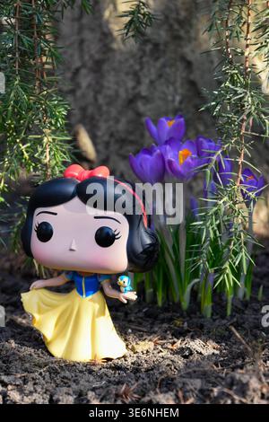 Funko Pop Actionfigur der Disney Prinzessin Schneewittchen mit Vogel. Erste Frühlingsblumen, blaue Krokusse blühen im Garten. Stockfoto
