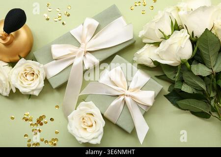 Komposition mit Geschenkboxen, weißen Rosenblüten und einer Flasche Parfüm auf grünem Hintergrund Stockfoto