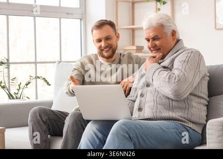 Junger Mann, der seinem älteren Vater zu Hause erklärt, wie man Laptop benutzt Stockfoto