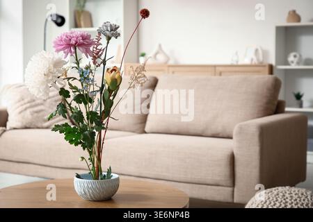 Topf mit wunderschönem Ikebana auf Couchtisch in stilvollem Wohnzimmer, Nahaufnahme Stockfoto