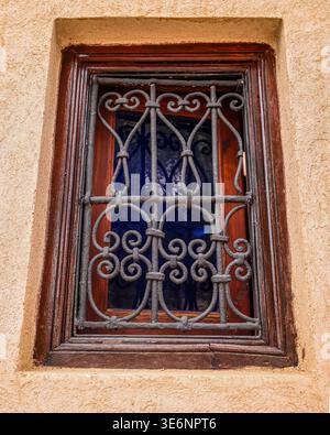 Kunstvoll verzierte schmiedeeiserne Fensterscheibe an der traditionellen Stuckwand in der Marrakesch Medina, Marokko Stockfoto
