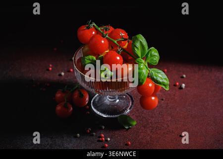 Tomaten und Basilikum auf dunklem Hintergrund mit Glasschale und verstreuten Gewürzen Stockfoto