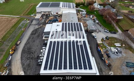 Mehrere Gebäude befinden sich in einer ländlichen Landschaft, auf deren Dächern Solarpaneele installiert sind. Felder sind im Hintergrund sichtbar, und Geräte sind im gesamten Bereich verstreut. Stockfoto