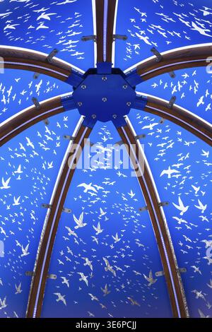 Nahaufnahme aus hinterleuchtetem blau getöntem Plexiglas und geschwungenen Holzpaneelen, die mit weißen Vogelschwärme in interaktiven Flugmotiven verziert sind Stockfoto