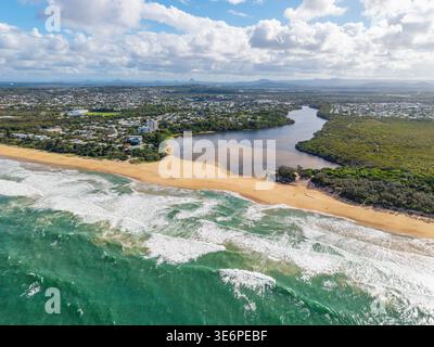 Ein Luftbild fängt den Currimundi Creek ein, der in den lebhaften Pazifik mündet, mit einem breiten Sandstrand und einer Küstenstadt. Stockfoto