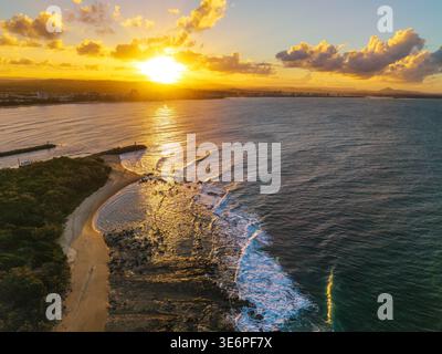 Aus der Vogelperspektive wird ein atemberaubender Sonnenuntergang über dem Pazifischen Ozean mit Blick auf die Mündung des Mooloolah River und den Point Cartwright Beach erfasst. Stockfoto