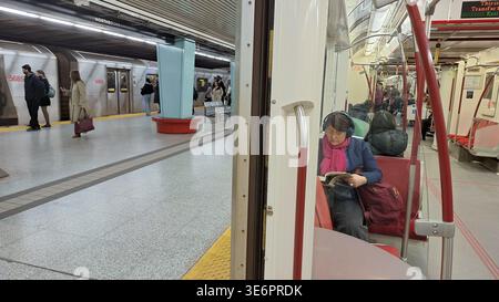 Toronto, ON, Kanada - 4. April 2026: Menschen, die auf U-Bahn warten, und Frauen, die ein Buch im Zug lesen, im Toronto Subway System, öffentliche Verkehrsmittel. Stockfoto