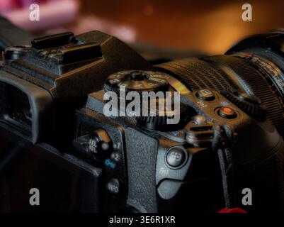 Nahaufnahme spiegelloser Kamerasteuerungen und Objektiv mit Modusrad und Aufnahmetaste in professionellen Fotogeräten für warme schlechte Lichtverhältnisse Stockfoto