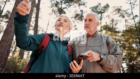 Wandern, altes Paar und Reisen mit Smartphone in den Wäldern, Reden oder Suche nach einem Standort auf der Website. Outdoor, Rucksacktouristen und ältere Menschen mit Stockfoto