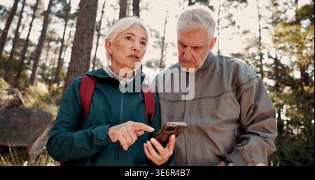 Wandern, altes Paar und Gespräch mit Smartphone im Wald, Verlorenen und Suche nach Ort auf der Website. Outdoor, Rucksacktouristen und ältere Menschen mit Stockfoto