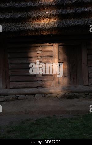 Sonnendurchflutete rustikale Holzhütte mit Strohdach und alter Tür Stockfoto