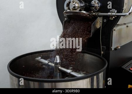 Dieses Bild zeigt den Moment, in dem geröstete Kaffeebohnen aus einem gewerblichen Kaffeeröster in eine Kühlschale gegossen werden. Die Bohnen sind dunkelbraun, ich Stockfoto