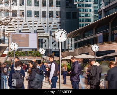 Büroangestellte gehen an Bahnhofsuhren in Canary Wharf, London vorbei. Das Finanzviertel ist während der Mittagspause im Frühling voll. Stockfoto