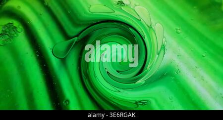 Grüne Flüssigkeit mit Ölblasen, die ein abstraktes Muster und einen wirbelnden Wirbel erzeugen Stockfoto