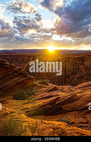 Sonnenuntergang über felsiger Schlucht mit Sandsteinklippen und dramatischen Wolken über Wüstengelände in der Abenddämmerung Stockfoto