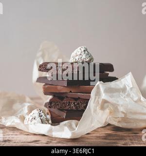 Stapel von verschiedenen Schokoladentafeln, einschließlich belüfteter dunkler und Milchschokolade, gepaart mit Gourmet-Trüffeln auf Pergamentpapier, selektiver Fokus Stockfoto