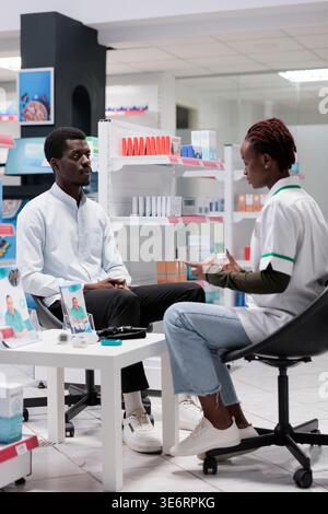 Apothekenberatung, Apothekenverkäufer, der Medikamente berät, Pillen-Paket halten. afroamerikaner und Sanitäter reden, Chemiker und Klienten Kommunikation, alles schwarzes Team Stockfoto