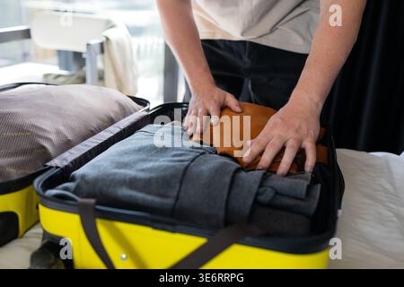 Mann, der ordentlich gefaltete Kleidung im blauen Koffer organisiert. Mann, der bestellte Kleidungsstücke in offenem Gepäck auf dem Bett platziert. Reiseplanung, Verpackungsroutine Stockfoto
