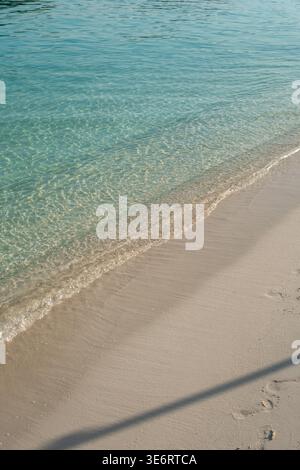 Minimale, menschenfreie Nahaufnahme einer sanften Welle über glattem Sand und klarem Flachwasser an der ionischen Küste in Ksamil, Albanien. Stockfoto