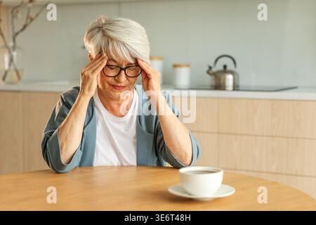 Kopfschmerzen. Unglückliche Seniorin mittleren Alters, die an Kopfschmerzen leidet, die sich zu Hause an den Schläfen reiben. Reife alte Großmutter berührt Schläfe und erlebt Stress Frau fühlt Schmerzen im Kopf Stockfoto