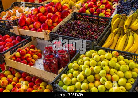 Eine lebhafte Präsentation von frischem Obst, einschließlich Äpfeln, Aprikosen und Bananen an einem Marktstand im Freien. Die Szene fängt die Fülle und Vielfalt von ein Stockfoto