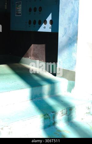 Abstrakte urbane Komposition von scharfem Sonnenlicht und Schatten auf einer verwitterten blauen Wand und türkisfarbenen Treppen in Ebisu, Tokio, Japan. Stockfoto
